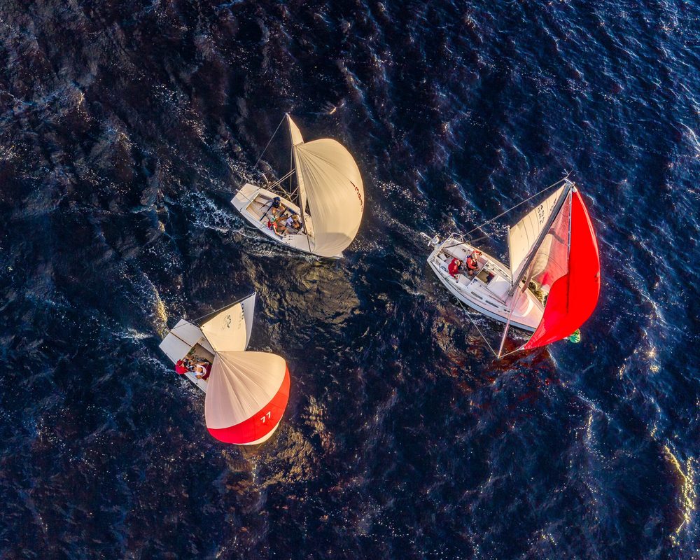 Three LMSA boats running downwind under spinnaker on Lake Monroe, seen from above in low evening light.